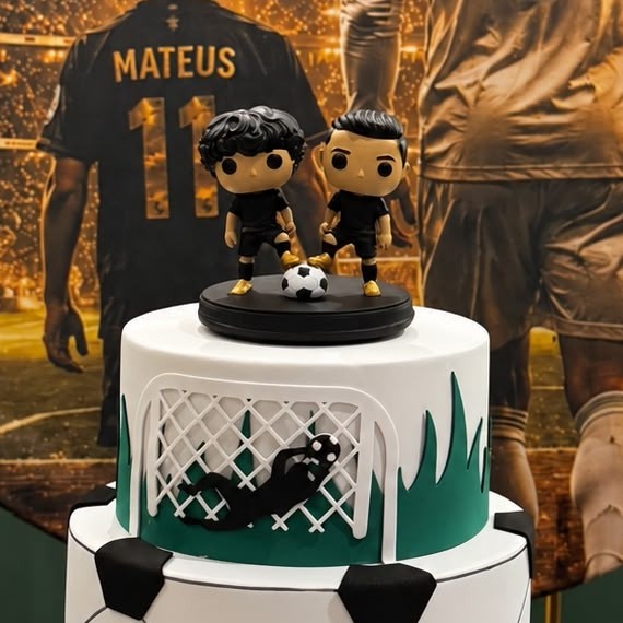 Dois bonecos de jogadores de futebol com uniforme preto e bola, sobre uma base no topo de um bolo de aniversário com tema de futebol